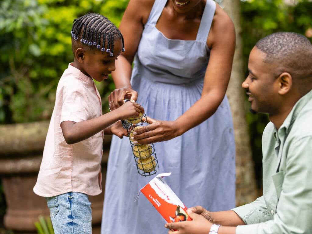 A family outdoors with a young child placing suet balls into a feeder.