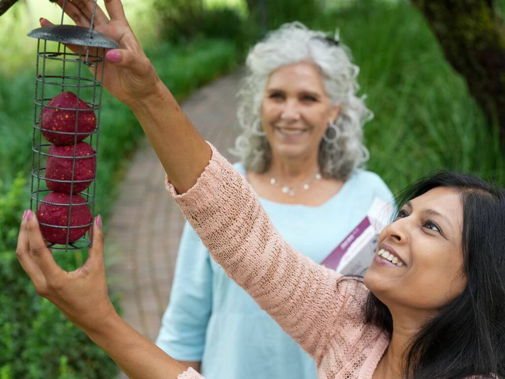 A woman smiles as she hangs a suet ball feeder filled with Berry Bliss Westerman’s suet balls.