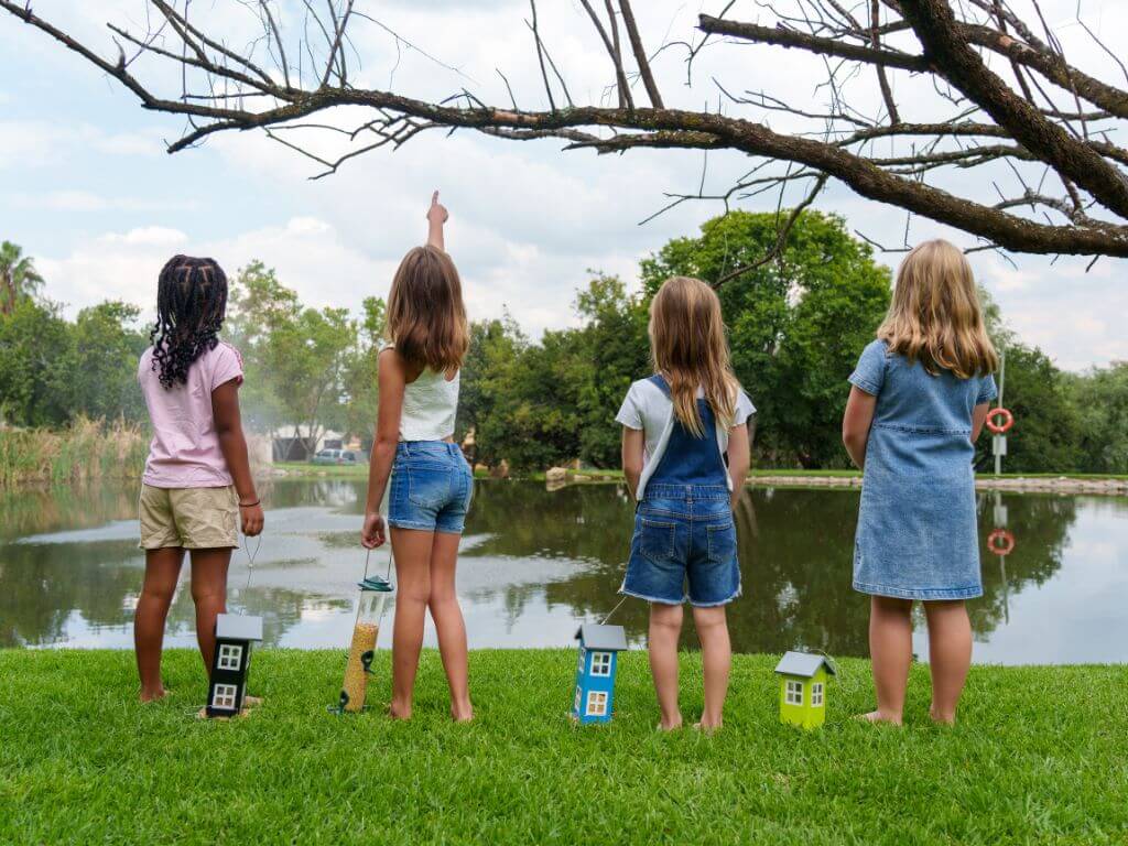 Four girls stand at the edge of a dam, holding Westerman’s bird feeders and looking up into the trees.