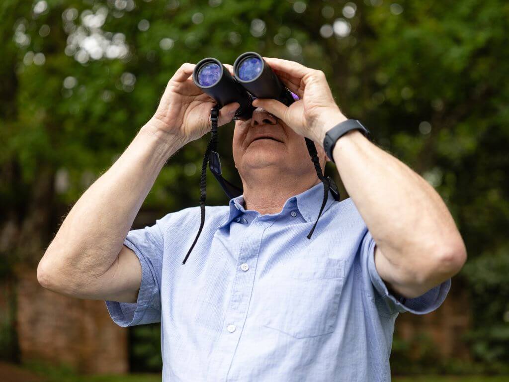 Man using binoculars to spot bird nests in a garden