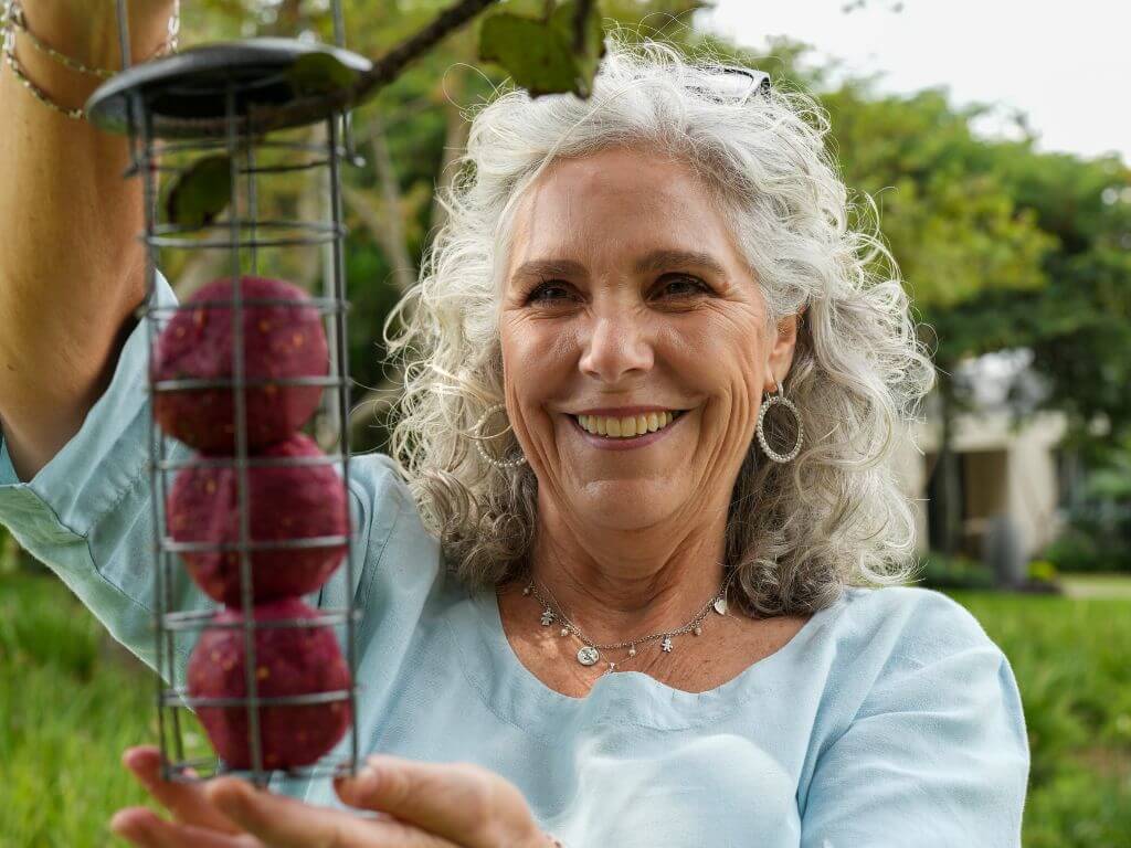 Smiling woman holding a feeder filled with Westerman's Berry Bliss suet balls, ready to hang for garden birds